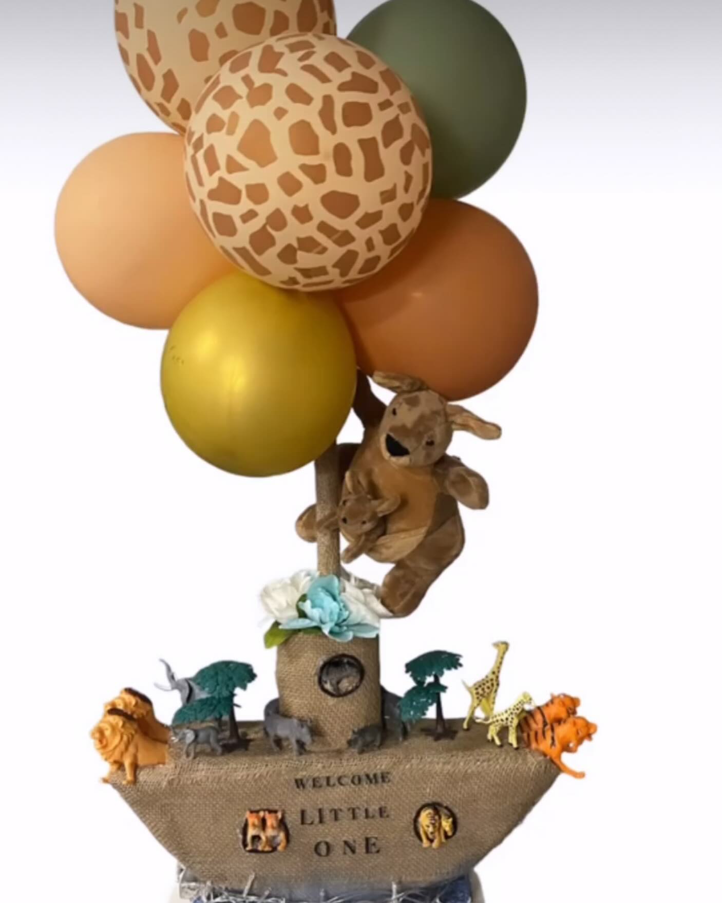 Noah's Ark themed centerpiece with plush animals, small toy animal figurines, greenery, and a balloon cluster in orange, yellow and green