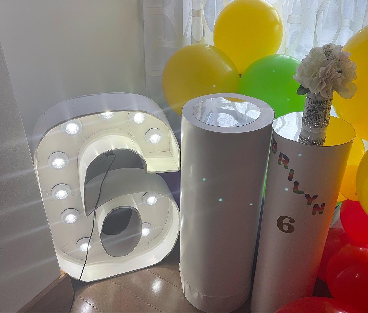Light-up marquee number '6' beside two round pedestal columns decorated with balloons and a floral topper