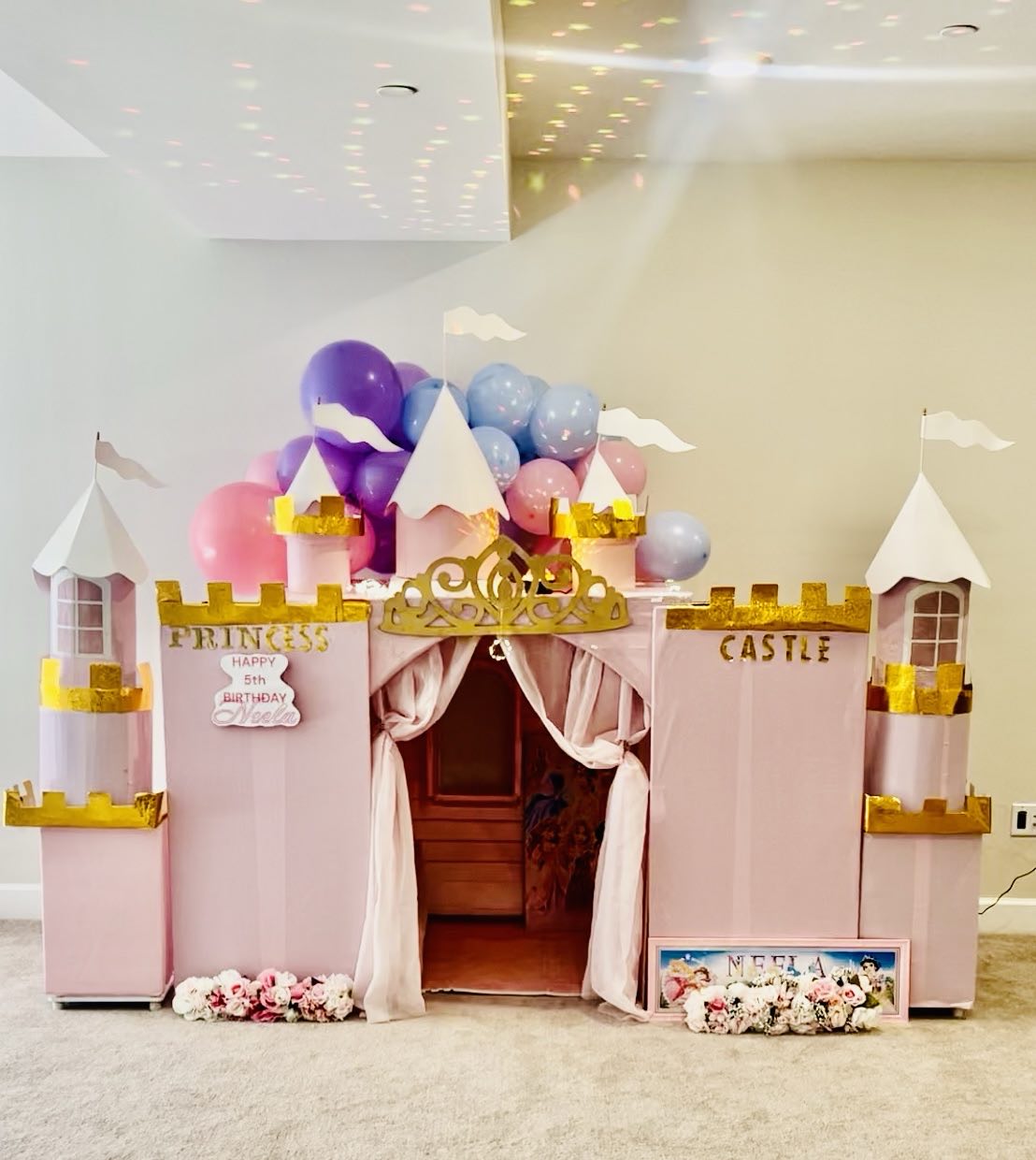 Pink and gold princess castle playhouse with turrets, gold crown, curtained doorway, balloon cluster on top and floral garland at the base