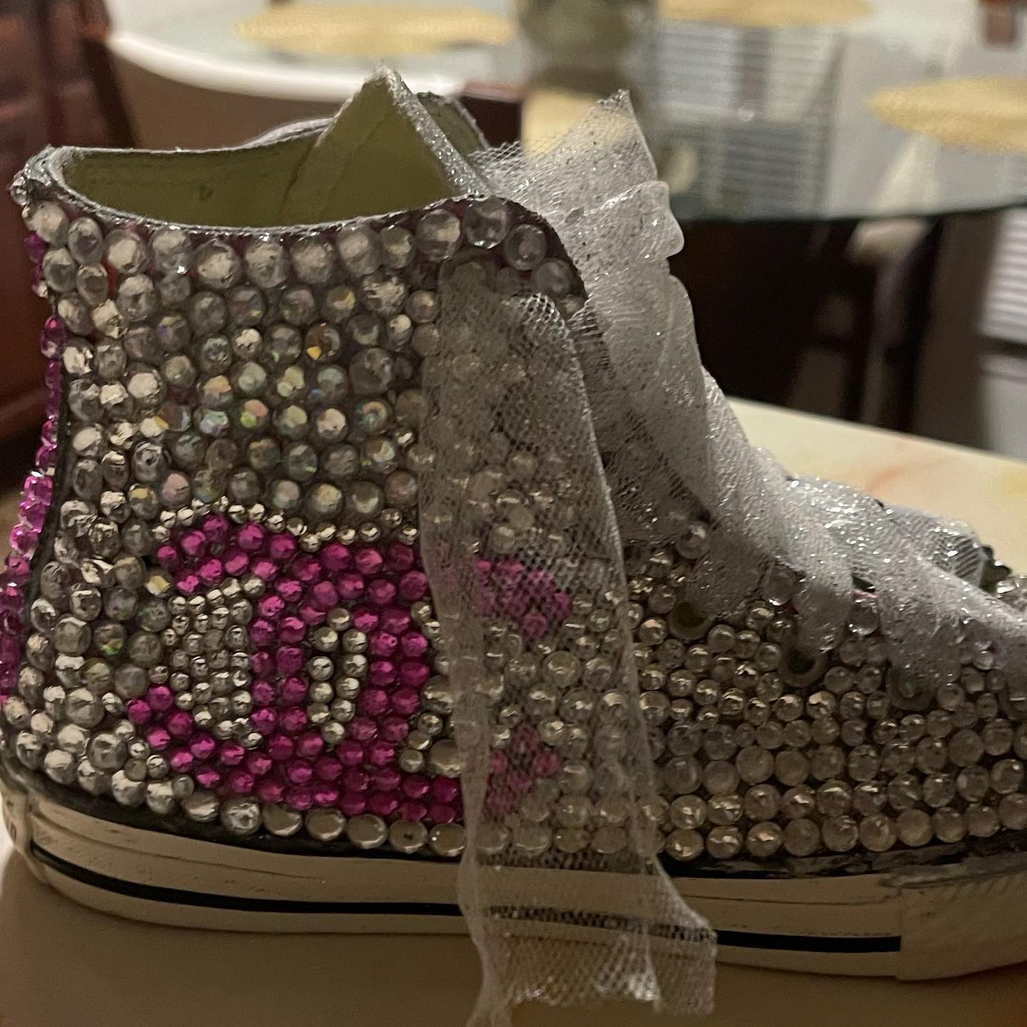 Close-up of a white high-top sneaker fully covered in clear and pink rhinestones with a sheer glitter ribbon lace