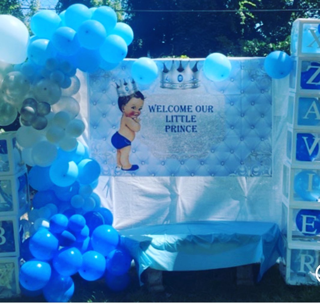 Blue 'Welcome Our Little Prince' baby shower backdrop with a crown, illustrated baby graphic, and blue and white balloon garland