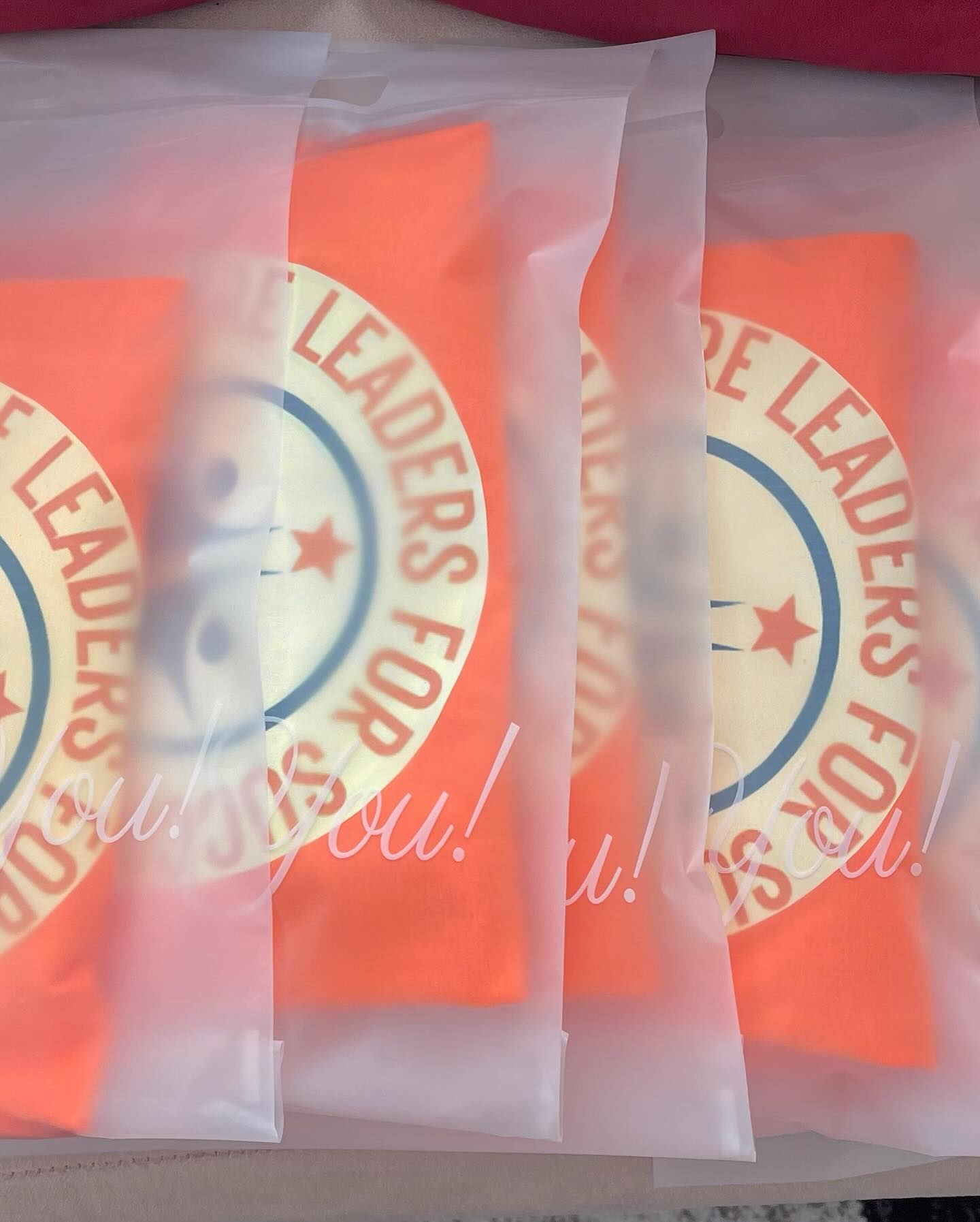 Close-up of folded orange t-shirts in clear packaging printed with a circular emblem logo and star design