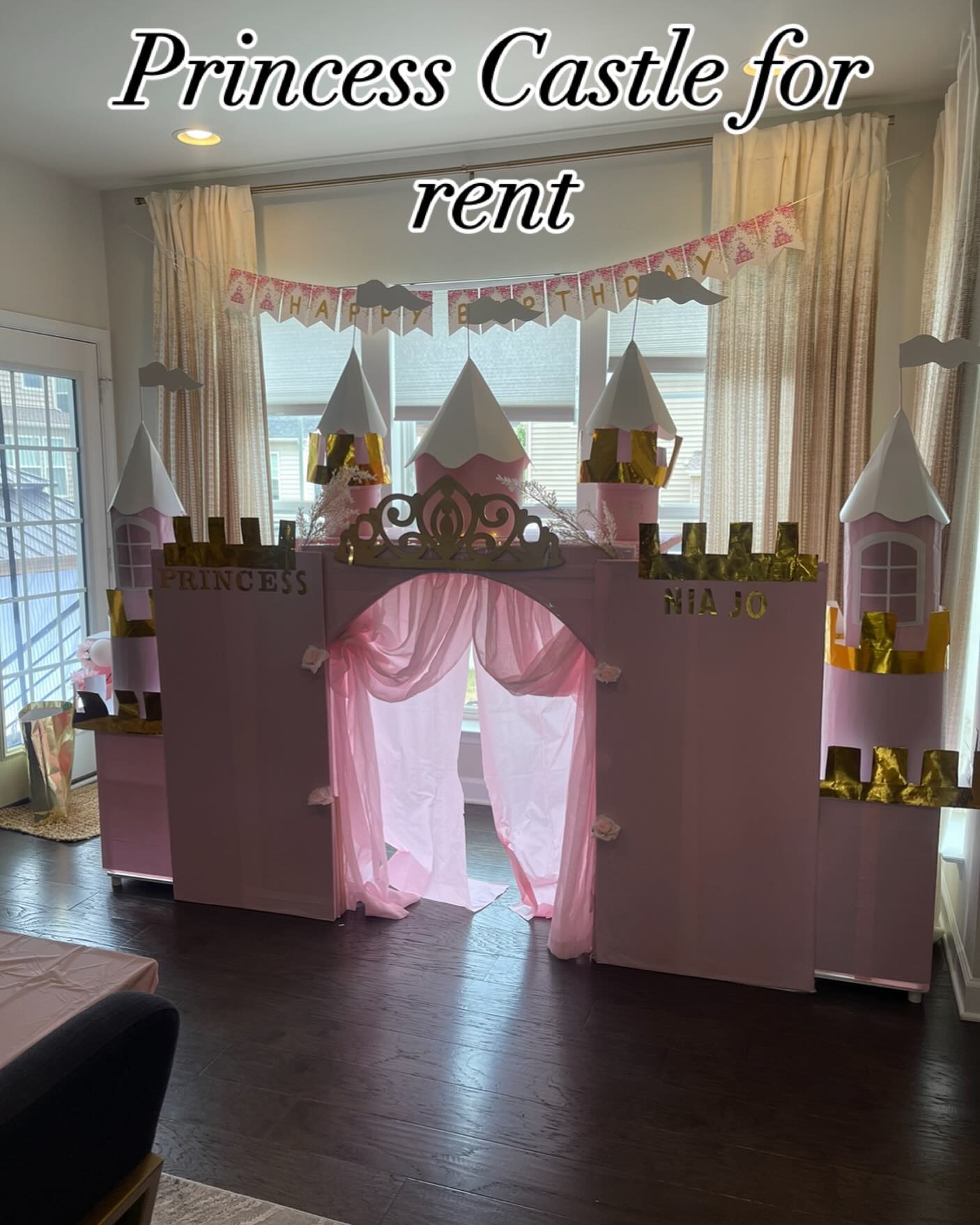 Pink and gold princess castle playhouse with turrets, gold crown, and a sheer curtained doorway in a living room with bay windows