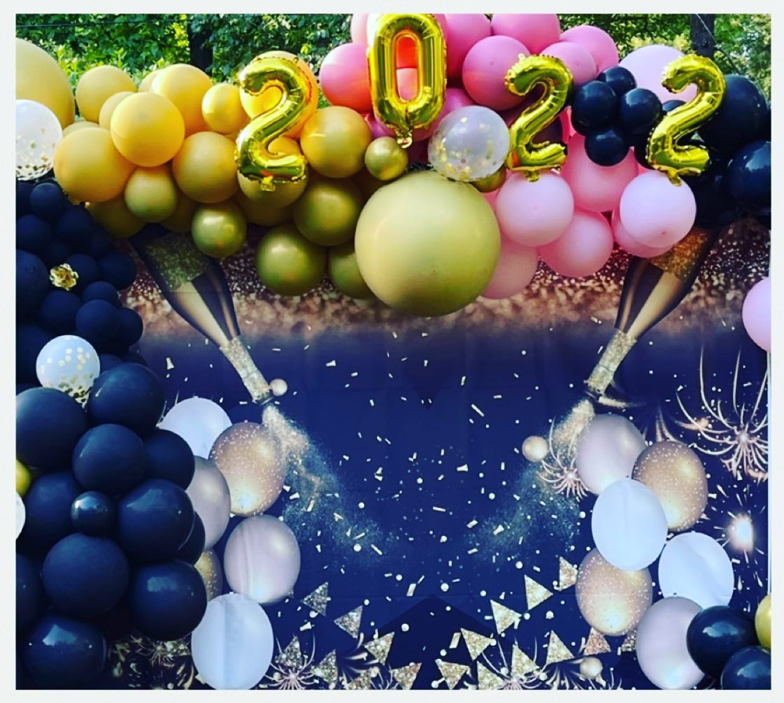 Balloon garland backdrop with gold 2022 number balloons, pink, olive, and navy balloons, and a graphic of champagne bottles popping with confetti