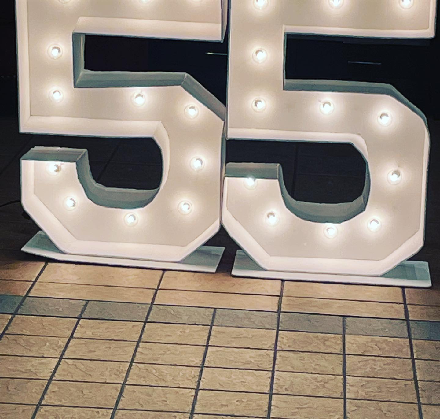 Two white light-up marquee number '5' fixtures with warm bulbs standing on a tiled floor