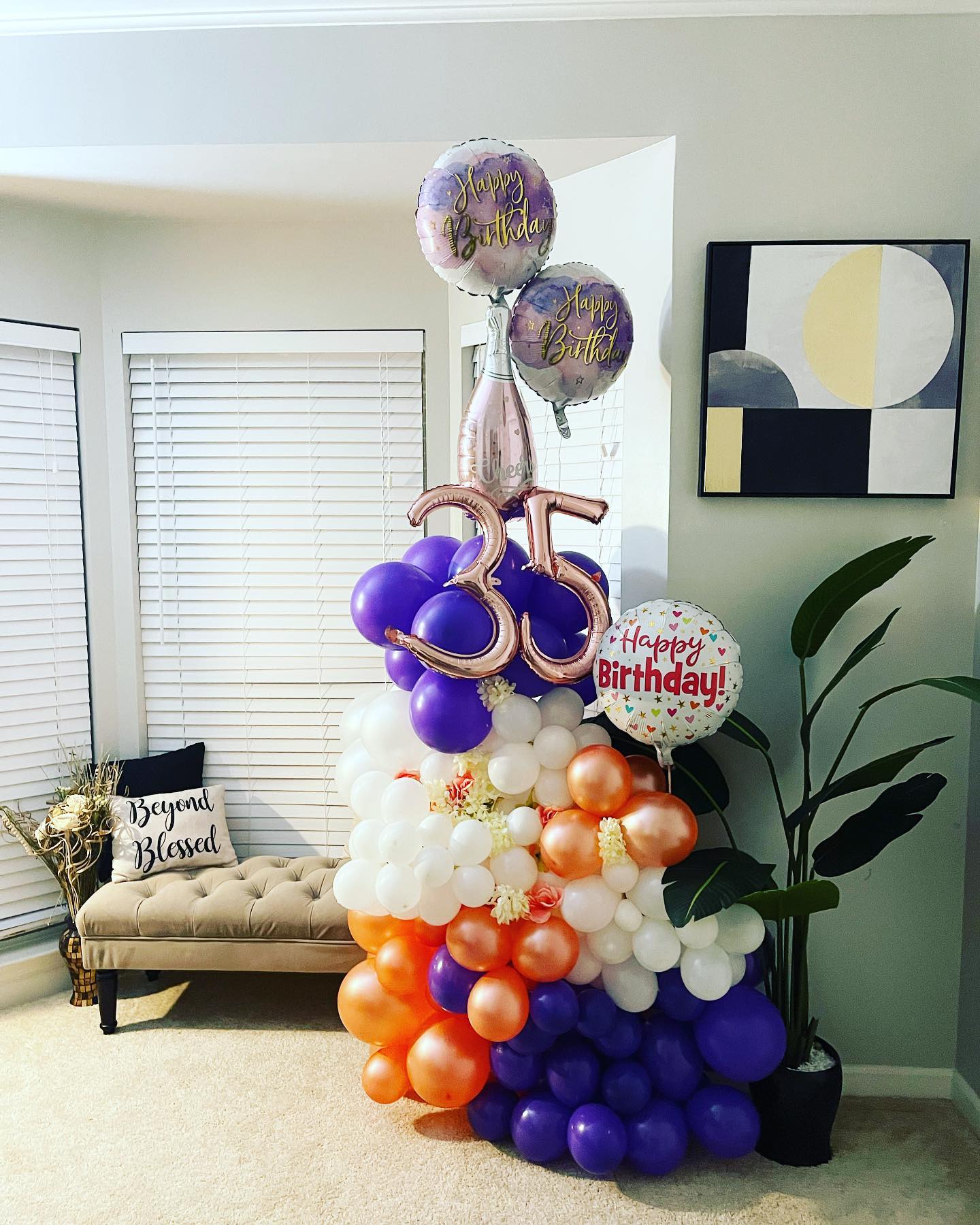 Purple, white and orange balloon column topped with number '35' balloons and 'Happy Birthday' foil balloons, in a living room